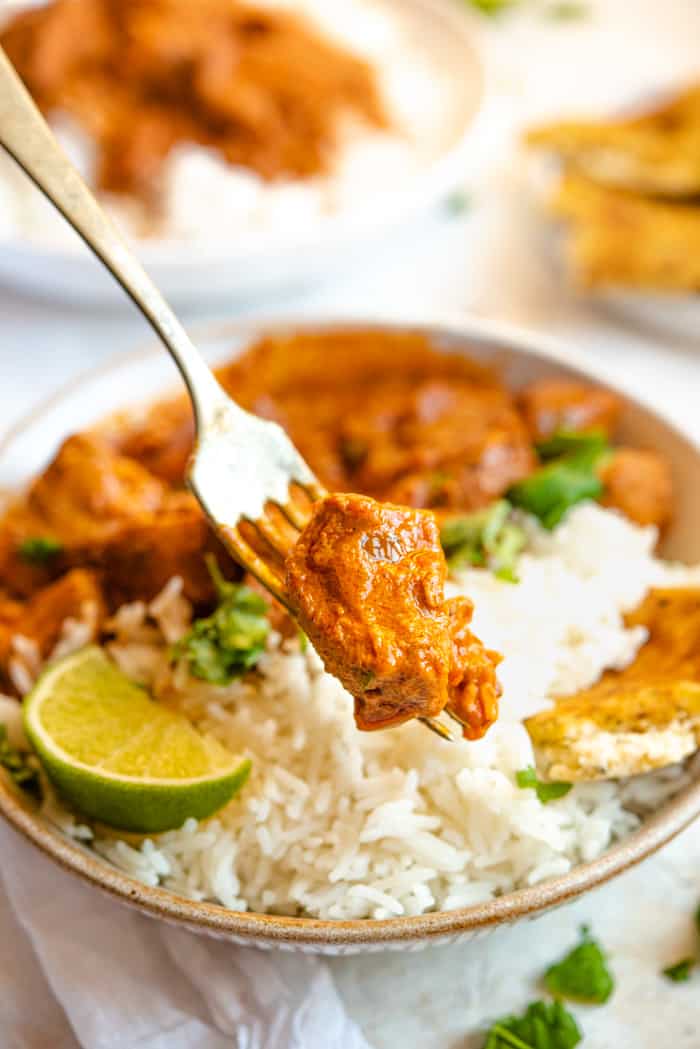 A close up of a piece of chicken curry on a fork