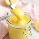 A close up of a spoon picking up some lemon curd from a jar.