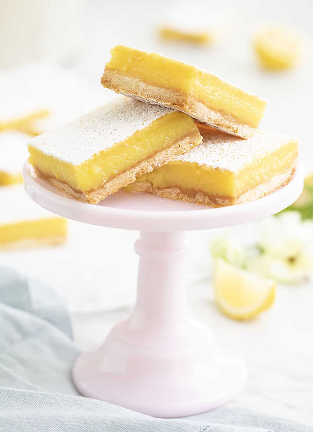 A group of lemon bars on a small pink cake stand.