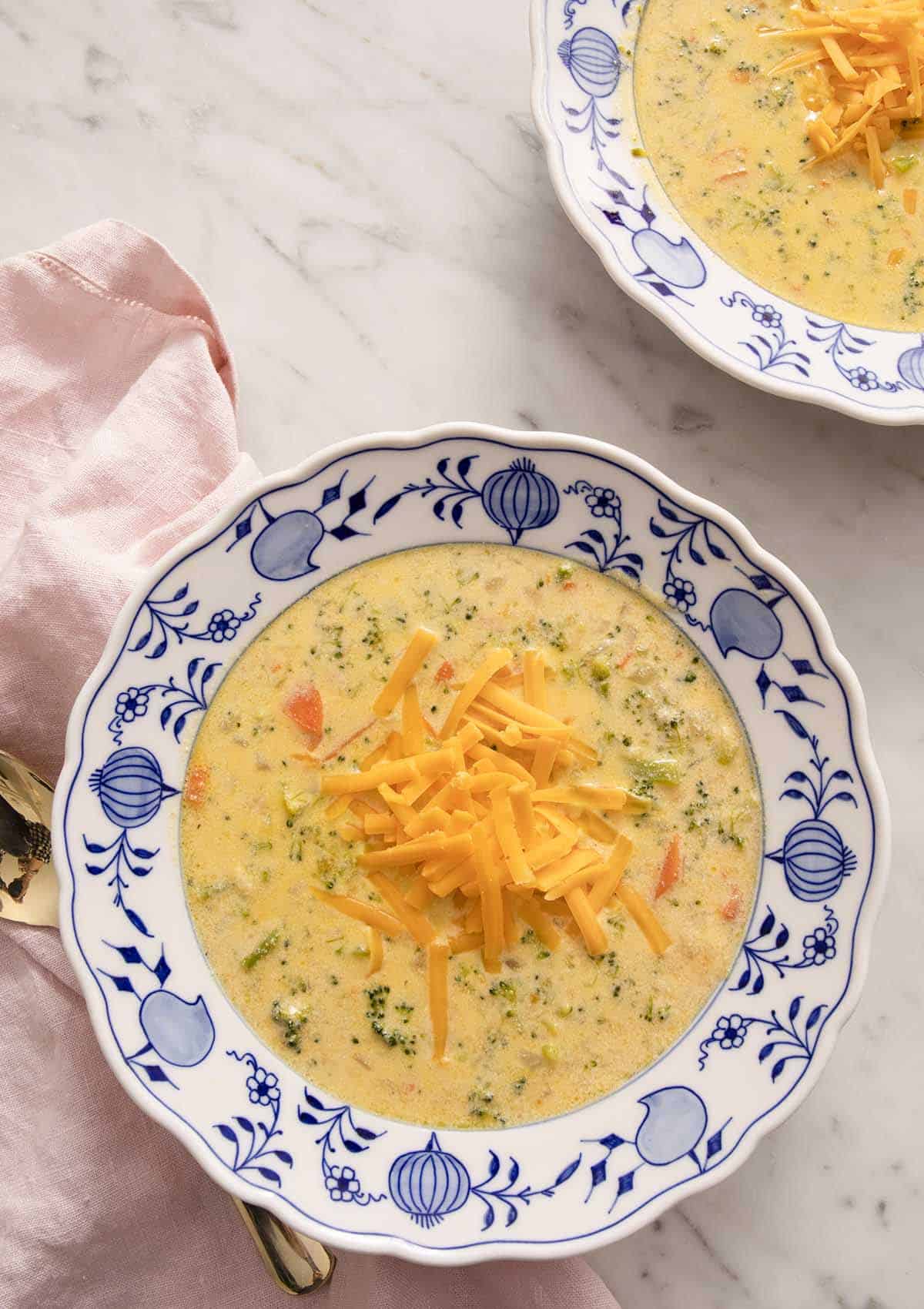 Two bowls of broccoli cheese soup on a marble table.