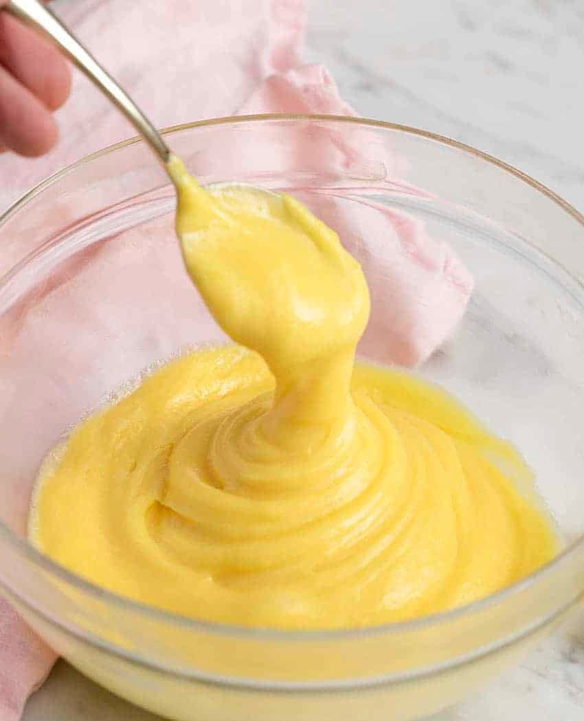 Freshly made lemon curd in a glass bowl rippling off of a golden spoon.