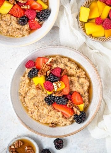 An overhead view of a bowl of Instant Pot steel cut oats topped with fruit and pecans. More toppings in bowls and a second bowl of oats on the side.