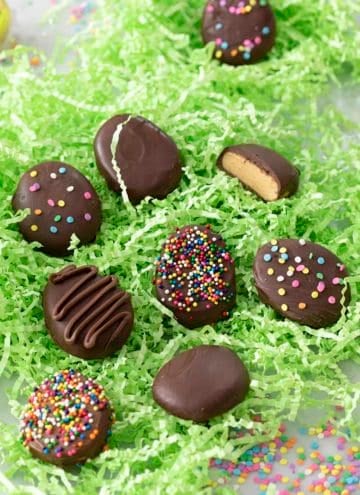 Peanut butter eggs covered in chocolate in a bed of green paper grass.