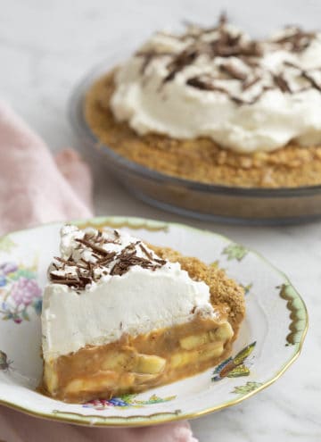 A piece of delicious banoffee pie in the foreground with the whole pie behind it.