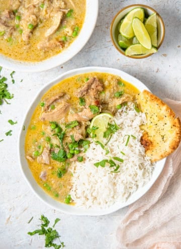 An overhead shot of chicken curry in a bowl with rice and naan. A bowl of lime wedges and just curry on the side.