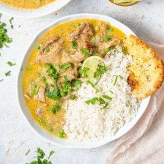 Overhead view of a bowl of Instant Pot chicken curry with rice, naan, lime wedges, and chopped cilantro.