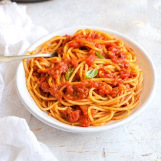 A white bowl of Instant Pot spaghetti sauce over pasta with some basil leaves.