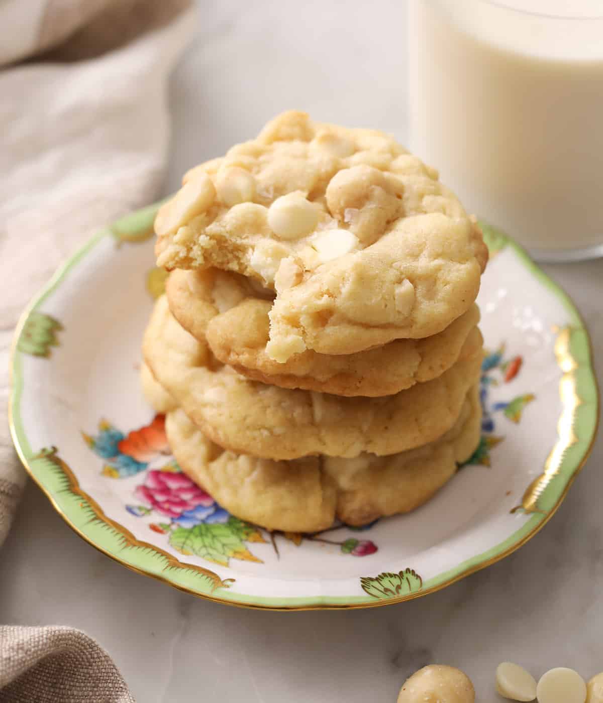 Stack of white chocolate macadamia nut cookies on a porcelain plate next to a glass of milk.