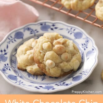 Pinterest graphic showing two white chocolate chip macadamia nut cookies on a blue and white plate.