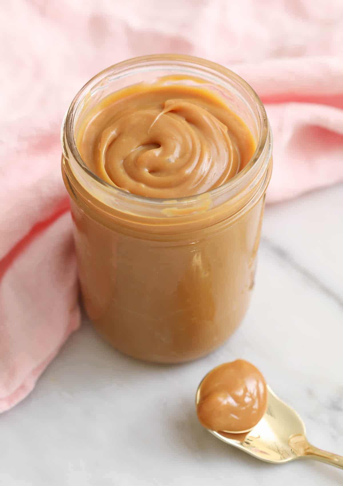 Golden dulce de leche in a glass jar next to a pink napkin.