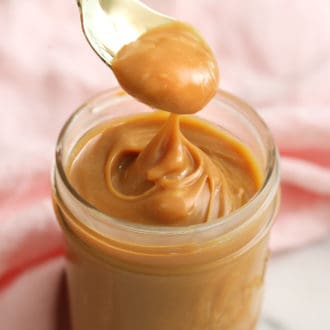 Silky dulce de leche getting spooned out of a glass jar.