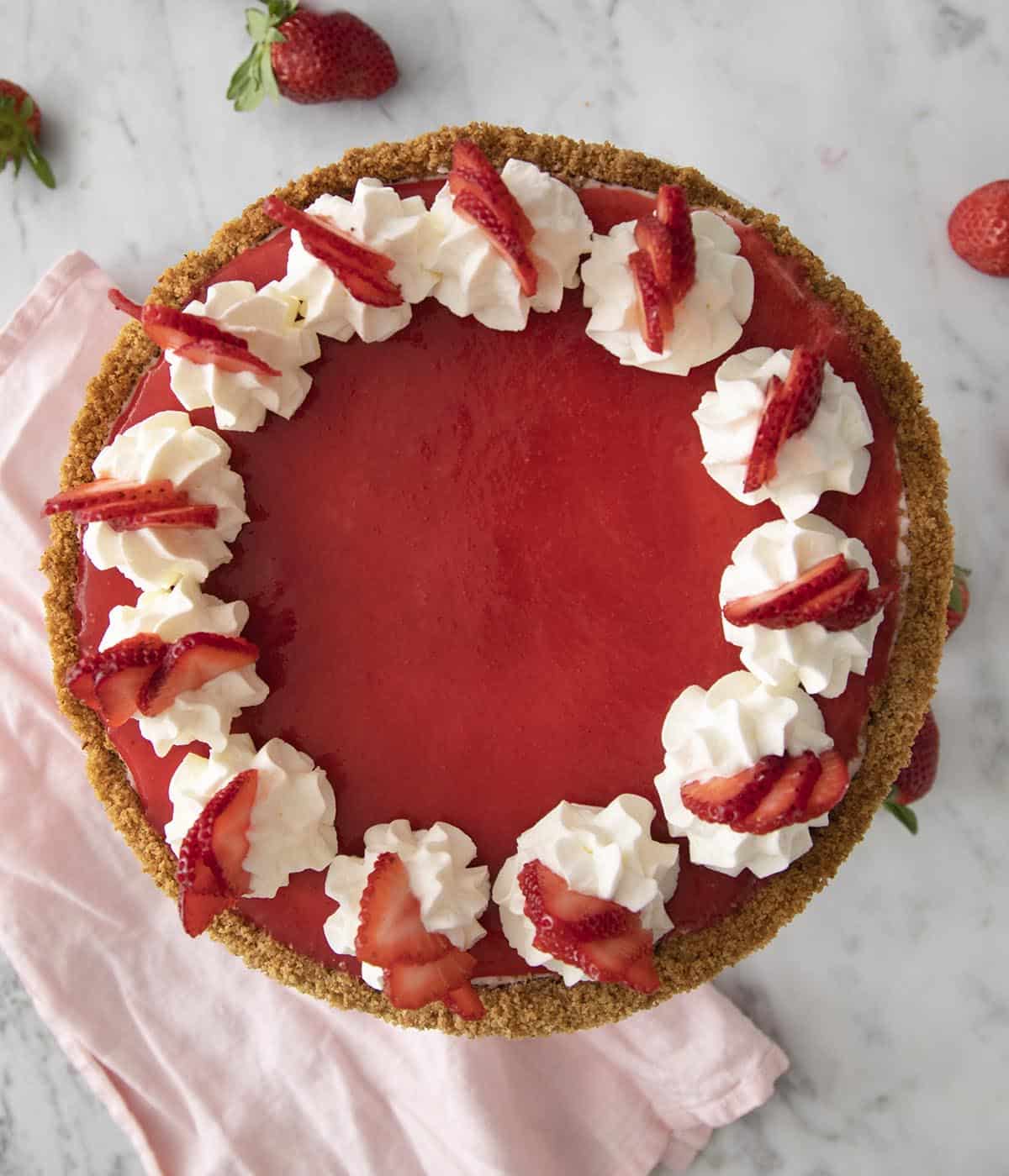 A top-down view of a beautiful no bake strawberry cheesecake with a ring of whipped cream dollops and strawberry slices on top.