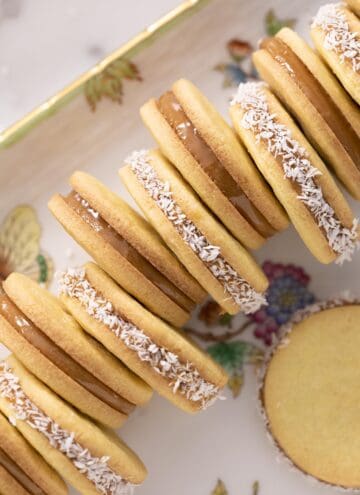 Alfajores on a porcelain serving tray, with every other one rolled in coconut.