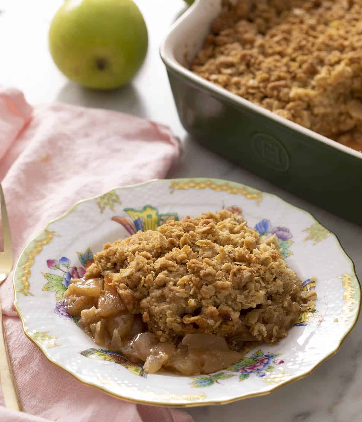 Apple crisp on a plate ready to eat. A baking dish with more apple crisp in the background.