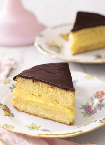 Two pieces of Boston cream pie on porcelain plates.
