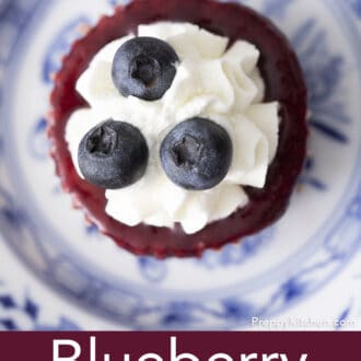 A top down photo of a blueberry mini cheesecake topped with a reduction and whipped cream on a plate.