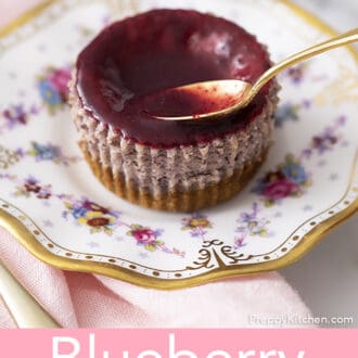 A gold spoon adding reduction to a Mini Blueberry Cheesecake.