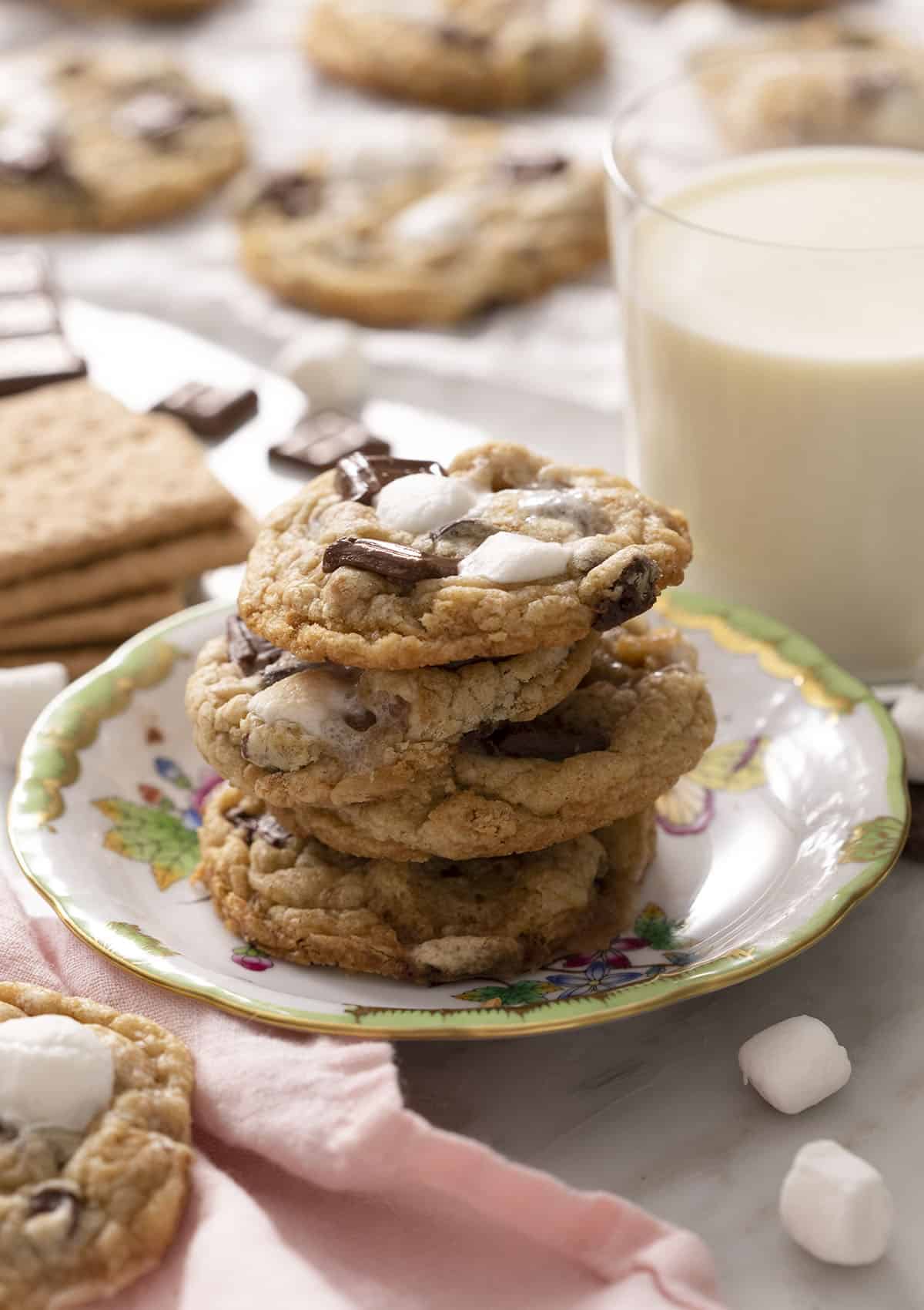 A stack of three s'more cookies on a plate with a glass of milk in the back.
