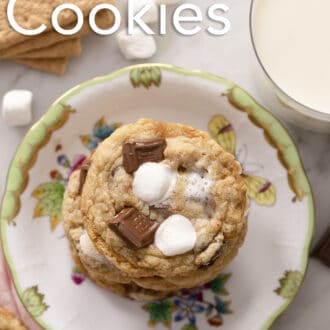 S'mores cookies stacked on a plate next to a glass of milk.