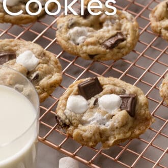 A glass of milk next to smores cookies on a copper rack.