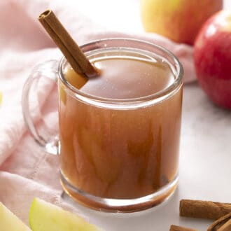 A glass mug of apple cider with a cinnamon stick inside.