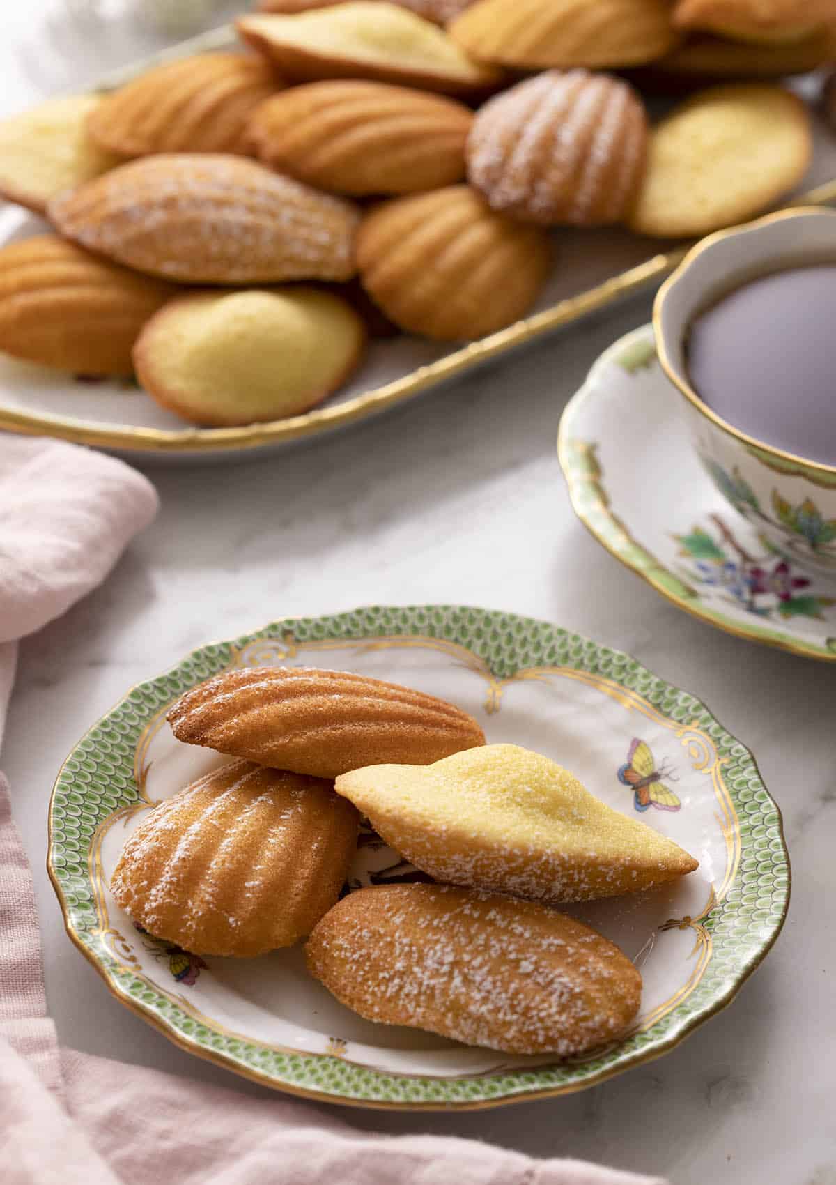 A green and white plate with Madeleines on a marble counter.
