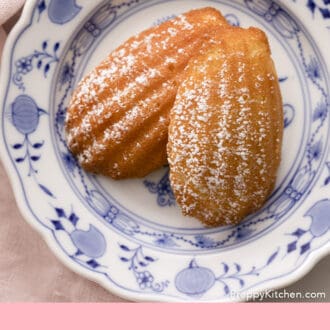 Pinterest graphic of two Madeleines dusted with powdered sugar on a blue and white plate.
