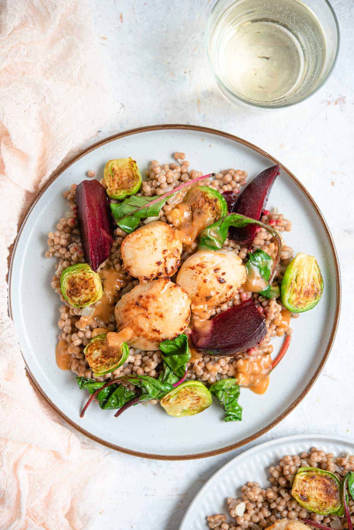 An overhead shot of 3 sauteed scallops on a plate with cous cous and veggies