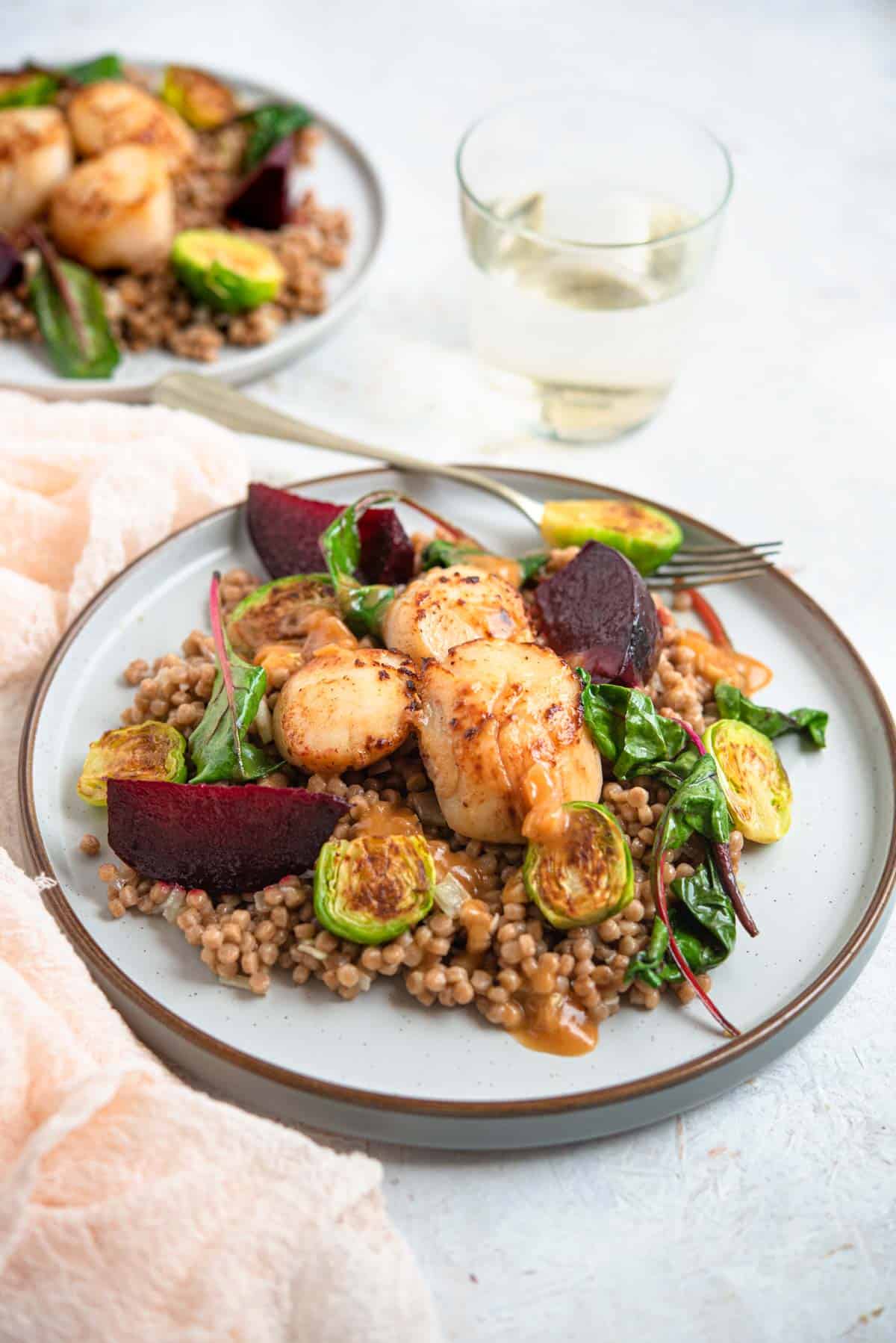 A side shot of sauteed scallops on a plate with cous cous and veggies