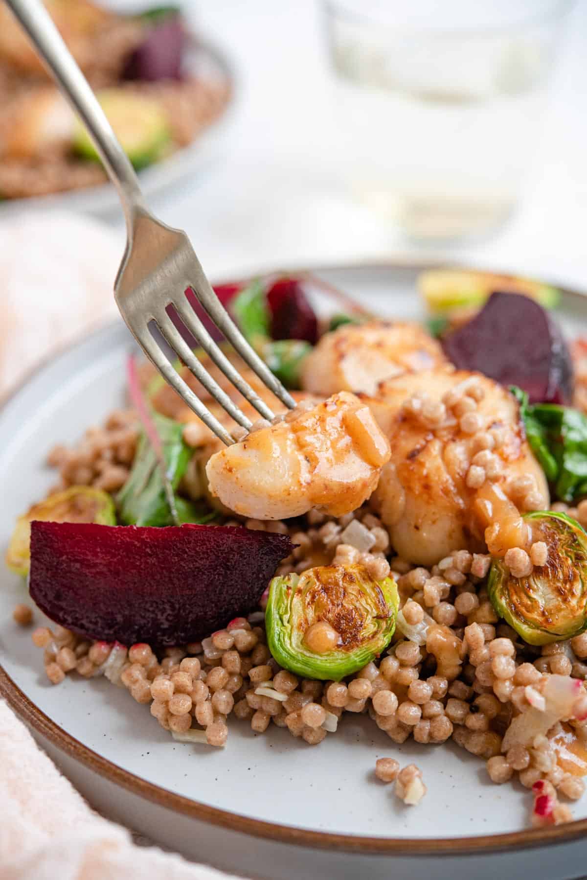 A close up of a fork picking up a scallop from a plate