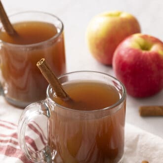 Pinterest graphic of two glass mugs of apple cider on a counter.