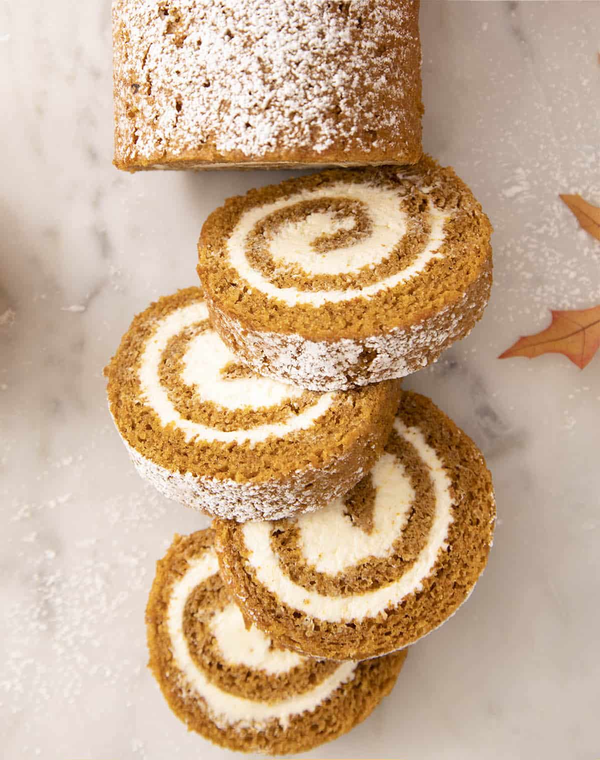 Pieces of pumpkin roll cake with four pieces sliced on a marble counter.