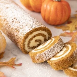 A pumpkin roll cake with three slices cut out.