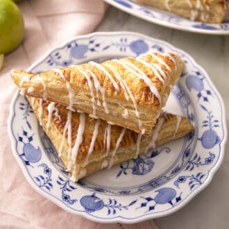 Two apple turnovers on a plate with glaze drizzled on top.