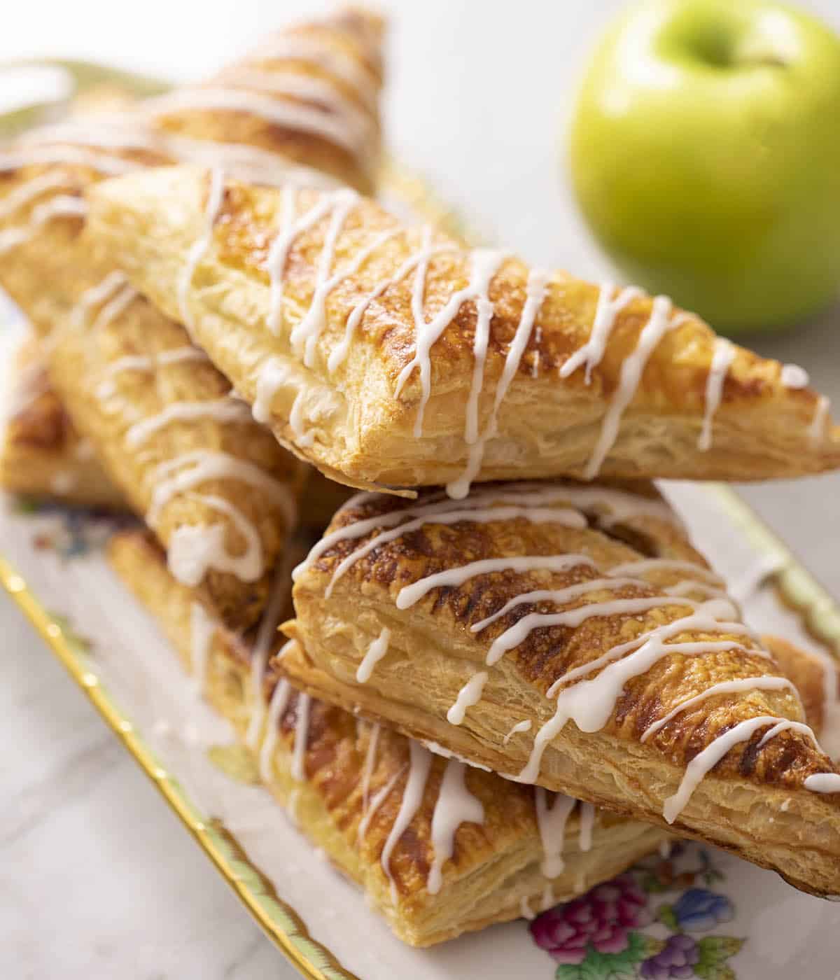 Flaky apple turnovers with glaze drizzled on top on a serving tray.