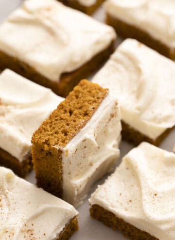 Pumpkin bars with cream cheese frosting on a marble counter.