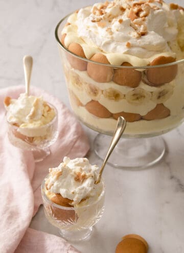 A banana pudding in a trifle dish with two portions in smaller serving glasses beside it.