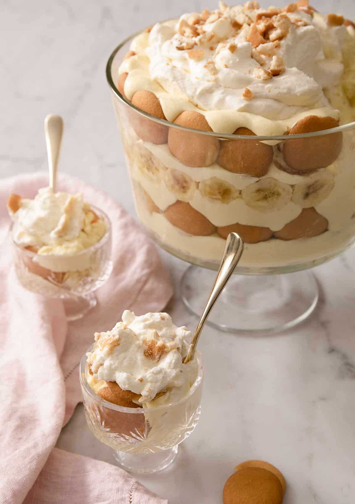 A banana pudding in a trifle dish with two portions in smaller serving glasses beside it.