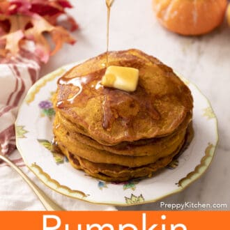 Maple syrup drizzling onto a stack of pumpkin pancakes on a porcelain plate.