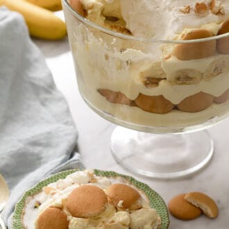 Banana pudding in a glass trifle dish. A serving on a plate in front of it.