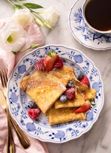 Folded crepes with berries and powdered sugar on a blue and white plate.