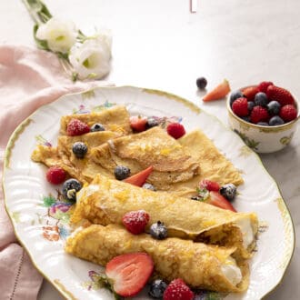 Pinterest graphic of rolled and folded crepes on a platter with berries.