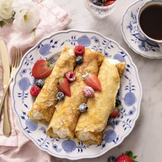 Pinterest graphic of rolled crepes on a plate with berries.