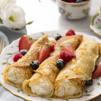 Pinterest graphic of rolled crepes on a plate with berries and citrus zest.