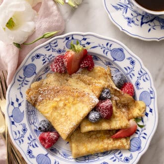 Pinterest graphic of crepes folded into quarters on a blue and white plate with berries.