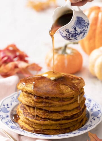 Maple syrup pouring onto a stack of pumpkin pancakes.