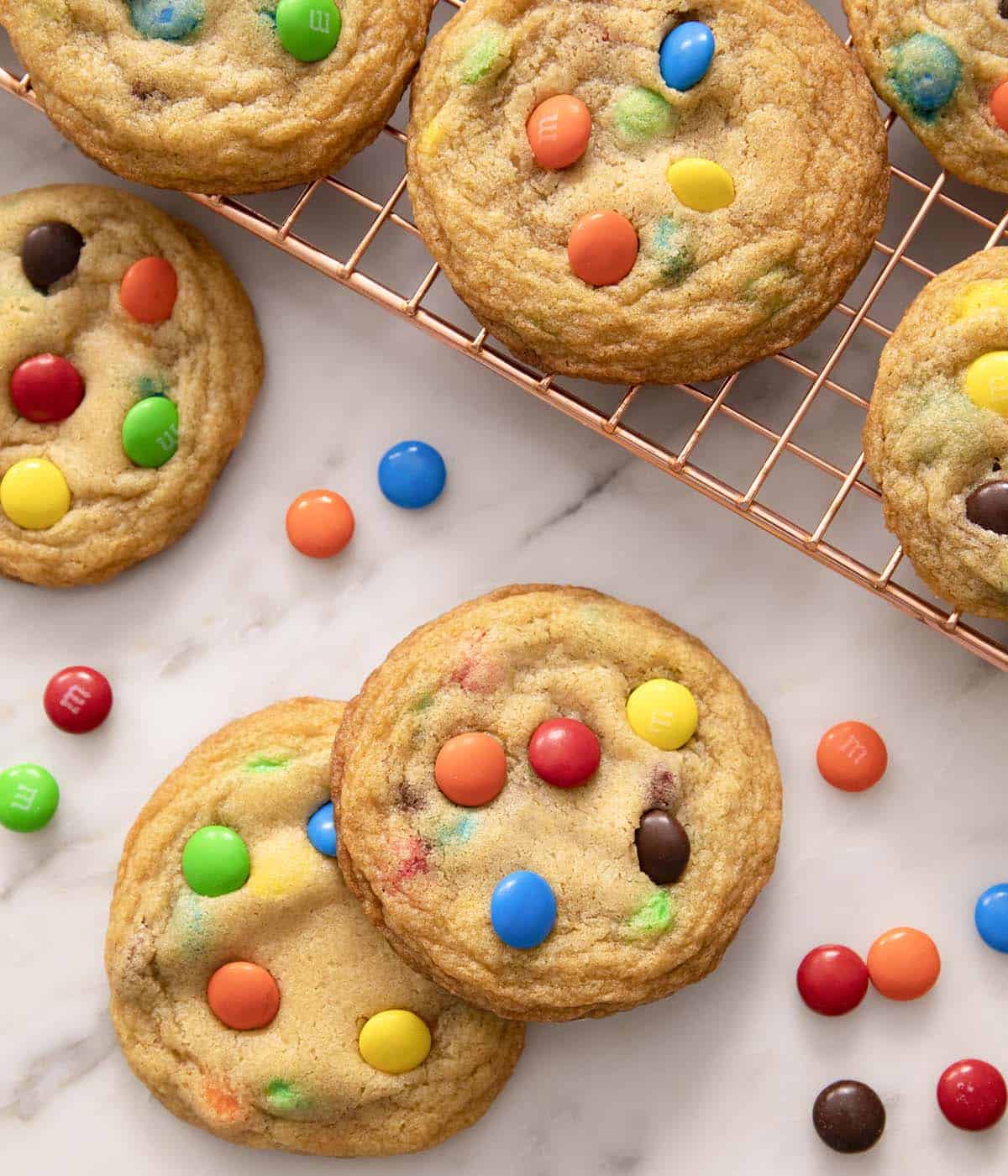 M&M cookies on a marble counter with more beside it on a cooling rack. 