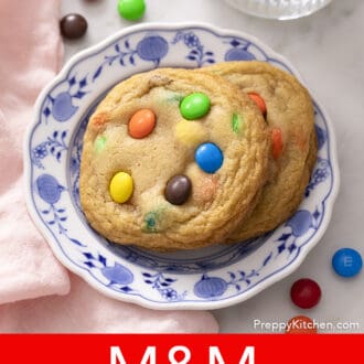 Pinterest graphic of overhead shot of 2 M&M Cookies on a blue and white plate.