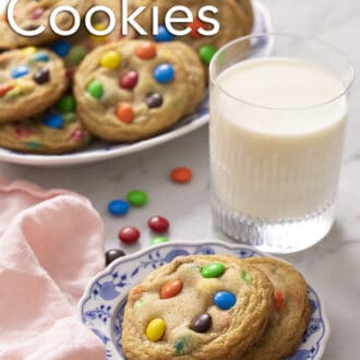 Pinterest graphic of 2 M&M Cookies on a blue and white plate with a glass of milk. More in the background.