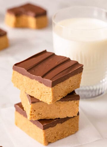 A stack of peanut butter bars on a marble surface alongside a glass of milk.
